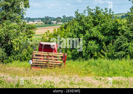 Campi di fattoria e alberi verdi in estate a Rivne, Ucraina villaggio di campagna con trattore di sgombero erbacce che tagliano grano e cielo blu Foto Stock