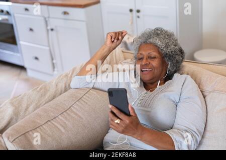 Donna anziana afroamericana sorridente mentre si ha una videochiamata sullo smartphone a casa Foto Stock