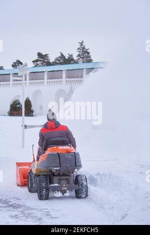 Russia, regione di Mosca, febbraio 2021. UN uomo vestito di calore su un aratro di neve rimuove la neve sul territorio del monastero in una giornata gelida. Foto Stock