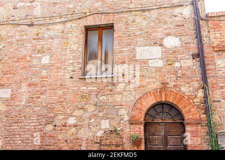 Chiusi, strada italiana nel piccolo borgo storico medievale della Toscana con chiocciatura di colorate pareti in pietra aranciata rossa e antica finestra in legno Foto Stock