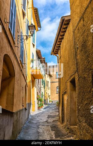 Chiusi, Italia vicolo scuro in piccolo borgo storico medievale in Toscana vista verticale durante il giorno con giallo arancio vivace Foto Stock