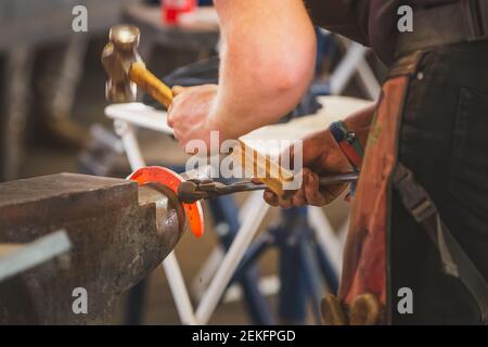 Primo piano di un fabbro ferriero che forgiava un ferro di cavallo rosso caldo. Foto Stock
