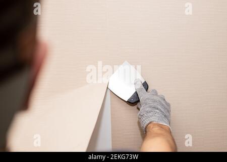 Man mano strappare la vecchia carta da parati chiaro da wall.Preparing per la riparazione a casa work.rimuovere carta da parati con una spatola, il processo di aggiornamento del muro Foto Stock