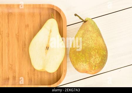 Una dolce matura succosa gustosa pera biologica Bere, su uno sfondo di legno naturale dipinto di bianco e una metà di una pera, su un vassoio di bambù Foto Stock