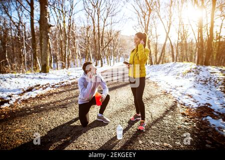 Vista laterale di giovani soddisfatti motivati e concentrati sportivi attivi coppia in sport invernali facendo una pausa con gli auricolari e. musica in un campo innevato Foto Stock