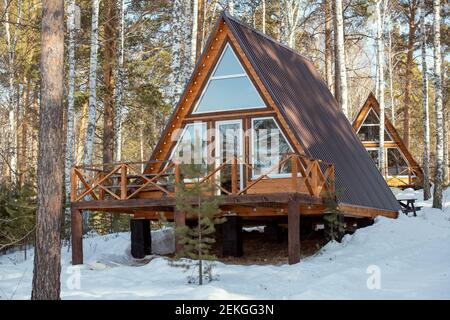Casa di campagna contemporanea in piedi nella neve nella foresta in davanti alla telecamera sullo sfondo di un'altra residenza tra i pini e birches Foto Stock