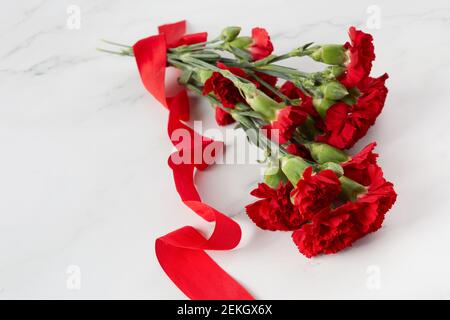 Fiori di garofano Beaytiful con nastro rosso su sfondo di marmo. Vista dall'alto Foto Stock