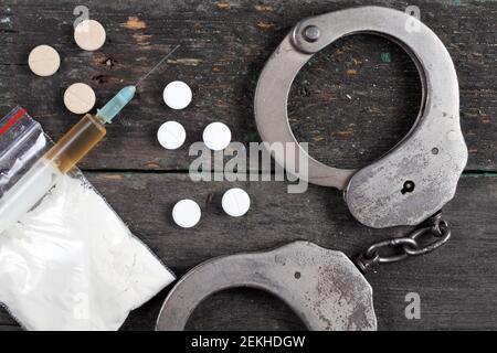 Siringa con cocaina e polsini di polizia su sfondo di legno scuro, vista dall'alto Foto Stock