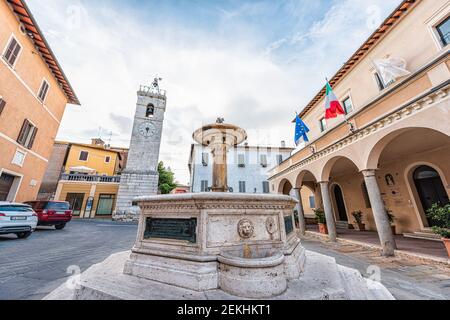 Chiusi, Italia - 25 agosto 2018: Piazza di strada in piccolo villaggio in Toscana durante il giorno con bandiere del municipio in centro e fontana storica Foto Stock