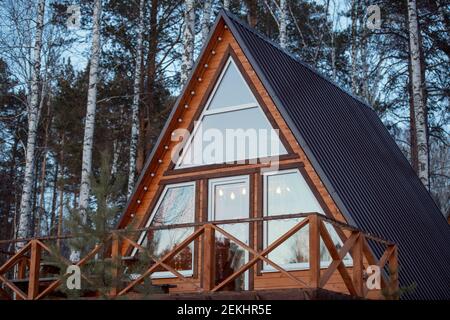 Nuova casa di campagna contemporanea grande in piedi in foresta mista in fronte della macchina fotografica sullo sfondo di pini e uccelli crescere insieme Foto Stock