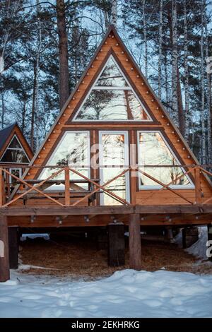 Grande casa di campagna in piedi nella neve di fronte alla macchina fotografica sullo sfondo di altra residenza tra pini e birch nella foresta Foto Stock