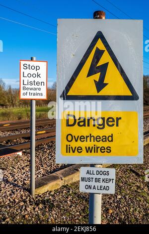 Pericolo in testa segnali di avvertimento per cavi sotto tensione in corrispondenza di un attraversamento di una ferrovia senza equipaggio nel Regno Unito. Stop Look Listen attenzione al segnale di avvertimento dei treni. Avviso di attraversamento. Foto Stock
