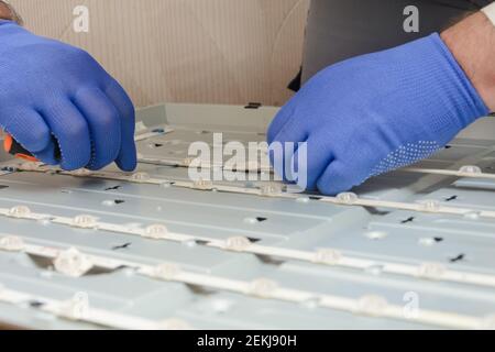 Mani di padrone in guanti installare la scheda LED sul pannello di grande TV nel centro di assistenza. Riparazione tv LCD, messa a fuoco selettiva. Foto Stock