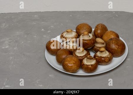 Grandi champignons reali su piastra bianca. Funghi marroni freschi per cucinare. Sfondo grigio in cemento. Foto Stock