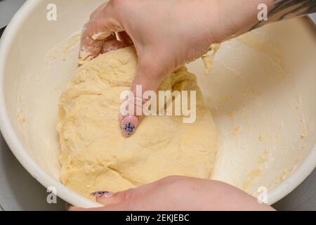 Produzione di pasta fatta in casa con farina bianca. Le mani delle donne impastano un pezzo di impasto per gnocchi o pasta. Primo piano, messa a fuoco selettiva. Foto Stock