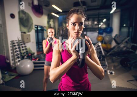 Due ragazze attive di forma atletica carina attraente sottile di forma giovane che fanno esercizi con kettlebells mentre si tiene capovolto nella palestra moderna. Foto Stock