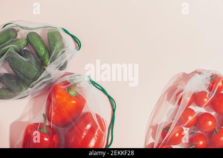 Imballaggio riutilizzabile dei prodotti in peso. Peperoni rossi, cetrioli e pomodori in una borsa riutilizzabile su sfondo rosa. Foto Stock