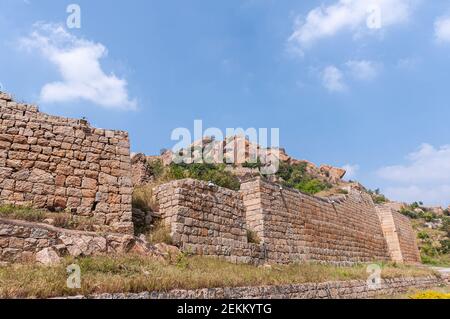 Chitradurga, Karnataka, India - 10 novembre 2013: Fort o Elusuttina Kote. Bastioni esterni in pietra marrone sotto il paesaggio blu nuvoloso con folliage verde e s. Foto Stock