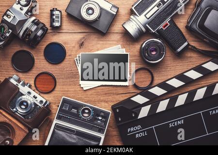 Fotocamera retrò d'epoca con clapboard e vecchie foto su sfondo di legno, tracciato di ritaglio Foto Stock