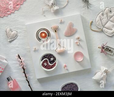 Rullo al quarzo in cristallo rosa e pietra Gua sha per la terapia del massaggio facciale, tessuto bianco e sfondo di cartone. Sale aromatico fatto a mano e. Foto Stock