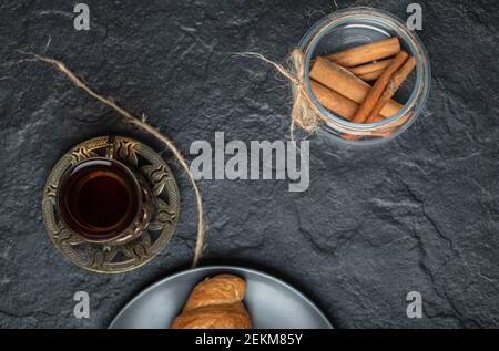 Un vaso di vetro pieno di bastoncini di cannella con una tazza di tè Foto Stock