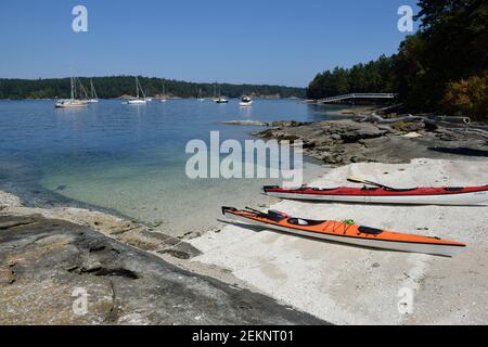 Kayak su una spiaggia conchiglia di fronte alle barche ancorate. Russell Island, British Columbia, Canada Foto Stock