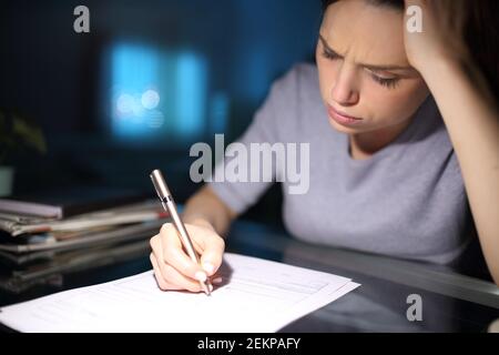 Donna preoccupata che riempiono il modulo di carta nella notte a casa Foto Stock