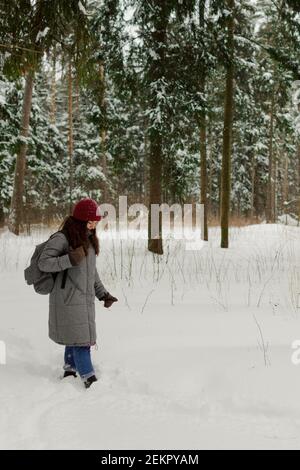 Una ragazza in un cappello rosso cammina nei boschi in una giornata nuvolosa, un sacco di neve. Foto Stock