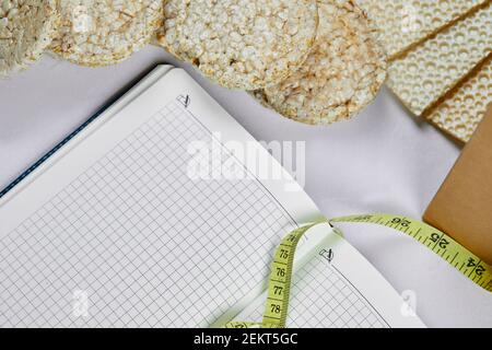 Cracker di riso, taccuino e metro a nastro su uno sfondo bianco Foto Stock