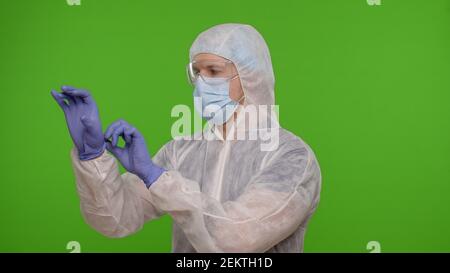 Medico lavoratore in tuta protettiva personale DPI preparazione e uso di guanti da mano su sfondo chiave cromatica. Attrezzature ospedaliere o cliniche durante il coronavirus, covid-19 quarantena pandemia blocco Foto Stock