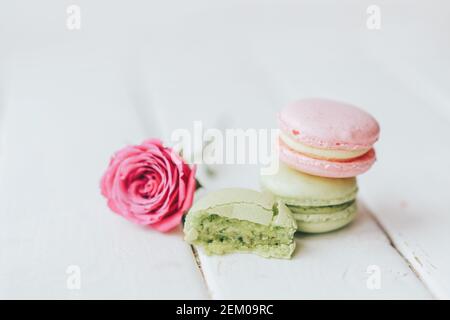 Su sfondo ligneo si trovano due macaroni, uno verde e l'altro rosa, e una bella rosa con mezzo macaroon davanti ad uno sfondo bianco. Foto Stock