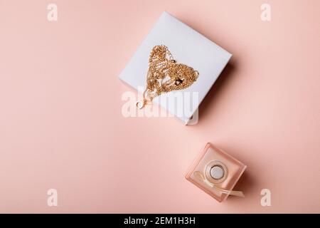 Un regalo per San Valentino. Profumo e una scatola con una catena d'oro su sfondo rosa. Foto Stock