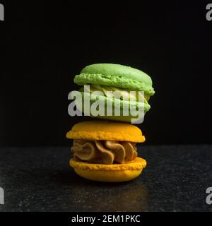 Macaron colorati impilati su una superficie scura, che evidenziano vivaci sapori verdi e gialli in una disposizione semplice Foto Stock