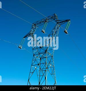 Linee elettriche ad alta tensione e torre di trasmissione contro un cielo azzurro limpido in una giornata di sole Foto Stock