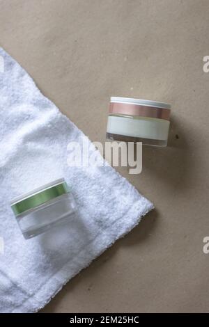 Due vasetti cosmetici in vetro con coperchio verde e rosa asciugamano e sfondo beige Foto Stock