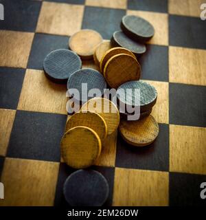 Classiche dama di legno su una scacchiera, con colori e pezzi diversi disposti a metà partita durante un piacevole pomeriggio Foto Stock