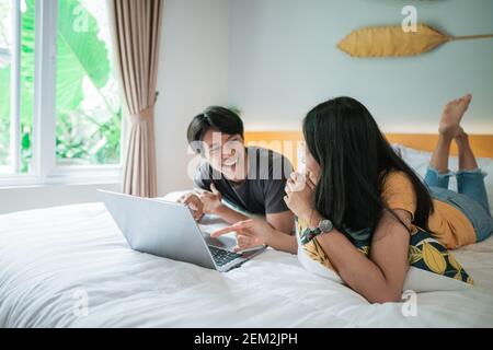 una coppia entusiasta che ride a letto utilizzando il computer portatile a casa in camera da letto insieme Foto Stock