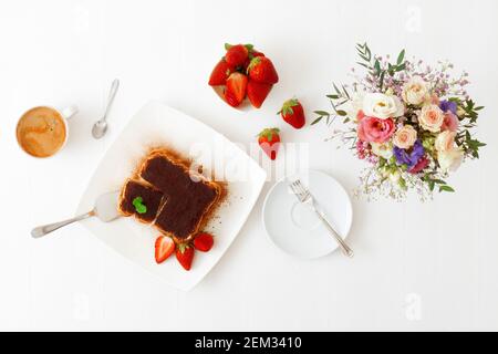 Tiramisù, dolce italiano fatto in casa senza forno dessert, taglio di torta su lama, abbellito con menta e alcune fragole reali, tazza di caffè, ciotola con st Foto Stock