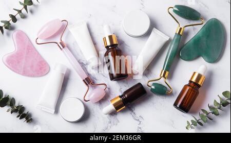 Prodotti cosmetici, oli essenziali, tubetti crema e rullo facciale su sfondo marmoreo Foto Stock