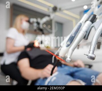 Focalizzazione selettiva sulla testa di perforazione dentale della nuova moderna macchina bur in studio dentistico, in primo piano. Manipolo dentale. Il medico e il paziente si sono offuscati sullo sfondo. Concetto di attrezzatura e strumenti di stomatologia Foto Stock