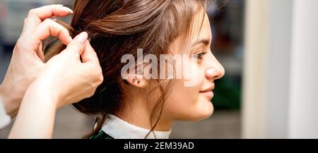 Vista laterale delle mani dei capelli stylist stylist di la bella giovane bruna caucasica in un salone di bellezza Foto Stock