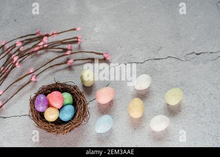 Uova di Pasqua colorate nel nido d'uccello con rami decorativi di salice su fondo grigio cemento Foto Stock