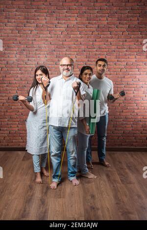 Famiglia indiana asiatica che si esercita a casa. Genitori anziani con bambini giovani che fanno yoga, sollevamento del peso, utilizzando theraband in soggiorno interno. Wor interno Foto Stock
