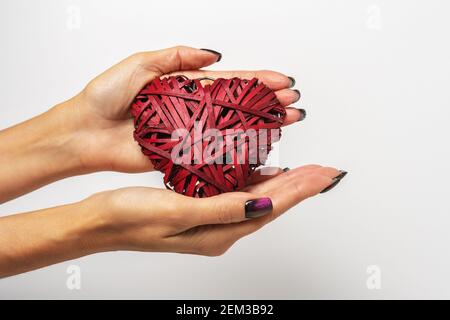 Cuore rosso di vimini fatto di paglia nelle mani della donna su sfondo bianco. Buon giorno di San Valentino o concetto di amore. Foto Stock