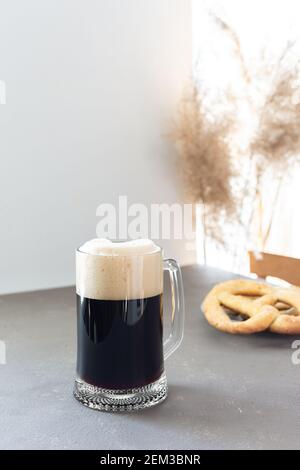 Birra artigianale scura in grande tazza di birra e deliziosa fatta in casa pretzel su sfondo grigio Foto Stock