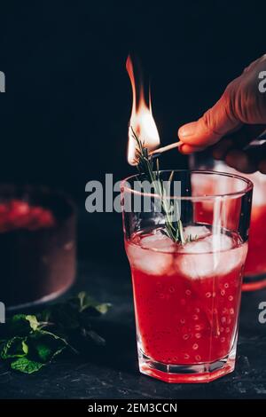 Composizione sorprendente con cheesecake alla fragola e bevanda alla fragola con rosmarino. Solo una parte della cheesecake a fuoco e una particella di un bicchiere di d Foto Stock