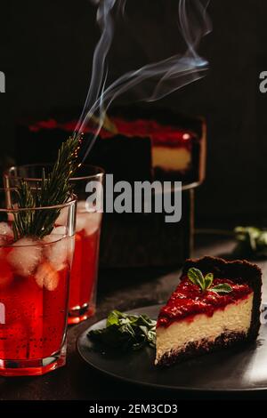 Composizione sorprendente con cheesecake alla fragola e bevanda alla fragola con rosmarino. Solo una parte della cheesecake a fuoco e una particella di un bicchiere di d Foto Stock