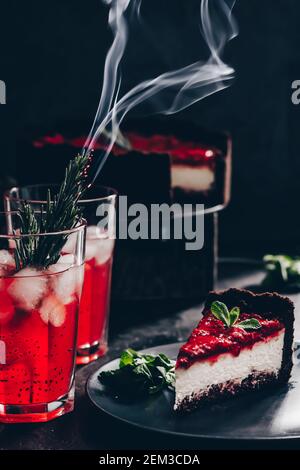 Composizione sorprendente con cheesecake alla fragola e bevanda alla fragola con rosmarino. Solo una parte della cheesecake a fuoco e una particella di un bicchiere di d Foto Stock