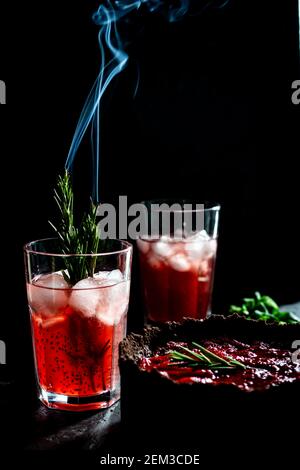 Composizione sorprendente con cheesecake alla fragola e bevanda alla fragola con rosmarino. Solo una parte della cheesecake a fuoco e una particella di un bicchiere di d Foto Stock