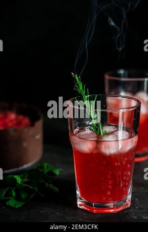 Composizione sorprendente con cheesecake alla fragola e bevanda alla fragola con rosmarino. Solo una parte della cheesecake a fuoco e una particella di un bicchiere di d Foto Stock